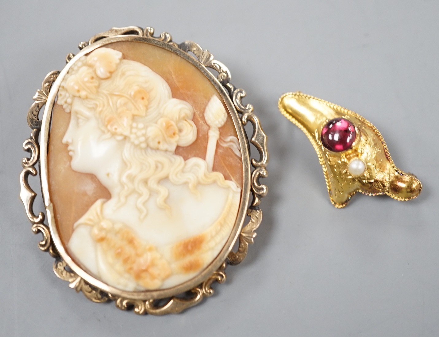 A yellow metal, garnet and seed pearl set brooch, 30mm gross 1.7 grams and a yellow metal mounted oval cameo shell brooch, 49mm, gross weight 10 grams.